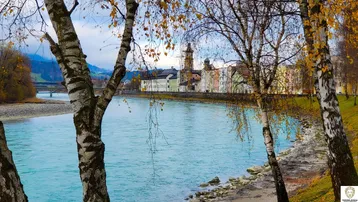 Malerischer Flusslauf mit herbstlichen Bäumen im Vordergrund und einer historischen Stadtkulisse am Ufer.