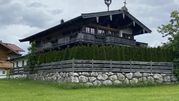 Traditionelles Holzhaus im alpenländischen Stil mit Steinfundament und gepflegter Hecke.
