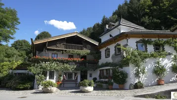 Traditionelles bayerisches Gebäude mit Holzbalkonen und üppiger Begrünung unter blauem Himmel.