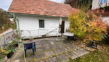 Hinterhof mit gepflasterter Terrasse, Gartenbereich und Blick auf das Haus mit Ziegeldach.