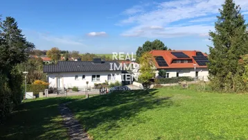 Weitläufiger Blick vom Grundstück auf die umliegende grüne Landschaft und benachbarte Häuser mit Solaranlagen.