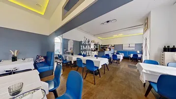 Geräumiger Restaurantbereich mit Holzboden, blauen Stühlen und weiß gedeckten Tischen, bereit für Gäste.