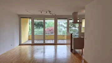 Heller Wohnbereich mit Holzboden, großen Fenstern und Zugang zu einem sonnigen Balkon.