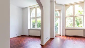 Helles Zimmer mit dunklem Parkettboden, weißen Wänden und eleganten Rundbogenfenstern.