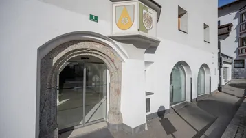 Historischer Eingangsbereich eines Gebäudes mit Steinbogen und modernen Glastüren an einer Straße.