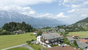 Panoramablick auf ein Wohngebäude in einer grünen Berglandschaft unter blauem Himmel.