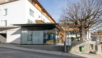 Modernes Gebäude mit Glasfassade und Holzelementen, gelegen an einer Straße mit altem Baumbestand.