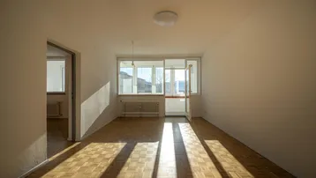 Helles Zimmer mit Parkettboden und großen Fenstern, das viel Sonnenlicht hereinlässt.