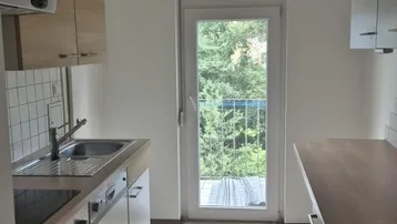 Helle Küche mit Holzarbeitsplatte, Einbauschränken und Zugang zu einem Balkon mit Grünblick.