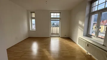 Heller Wohnraum mit Laminatboden, Heizkörper und Zugang zu einem kleinen Balkon mit Aussicht.