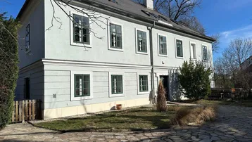 Historisches Gebäude mit heller Fassade, grünen Fensterrahmen und gepflegtem Vorgarten.