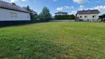 Großes, sonniges Grundstück mit Rasenfläche, umgeben von Wohnhäusern und Hecken.