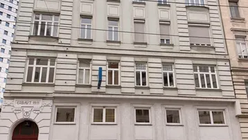 Klassisches Mehrfamilienhaus mit historischer Fassade, vielen Fenstern und parkenden Autos davor auf der Straße.