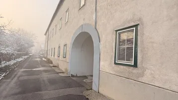 Langes, altes Gebäude mit Putzfassade und einem Torbogen an einem nebligen Wintertag.