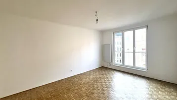 Leeres Zimmer mit Fischgrätparkettboden und großem Fenster mit französischem Balkon.
