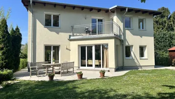 Großzügige Terrasse mit Gartenmöbeln und Zugang zum gepflegten Rasenbereich hinter dem modernen Haus.