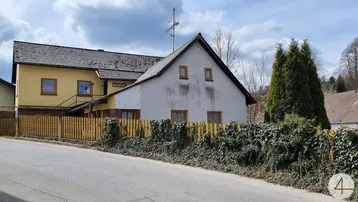 Seitenansicht eines älteren Hauses mit gelber und weißer Fassade sowie einem Holzzaun.