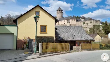 Gelbes Haus mit Blick auf eine historische Burg und ländliche Umgebung unter blauem Himmel.
