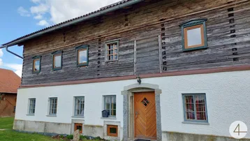Traditionelles Bauernhaus mit Holzbalken und weiß verputzter Fassade unter blauem Himmel.