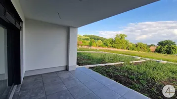 Unmöblierte Terrasse mit Fliesenboden und Blick auf die grüne Hügellandschaft unter blauem Himmel.