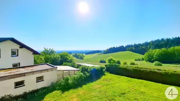 Weitläufiger Blick über grüne Hügel und Wälder unter strahlend blauem Himmel.