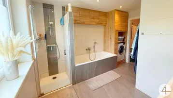 Modernes Badezimmer mit Dusche, Badewanne und integriertem Waschmaschinenbereich, hell gefliest.