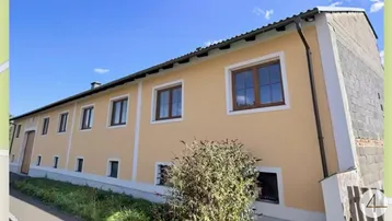 Gebäudeaußenansicht mit hellgelber Fassade und braunen Fenstern unter blauem Himmel.