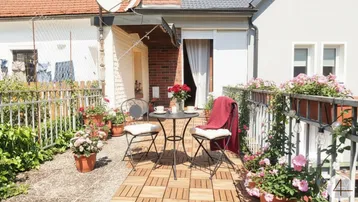 Gemütliche Terrasse mit Holzboden, Gartenmöbeln und vielen Blumen, ideal für entspannte Stunden im Freien.
