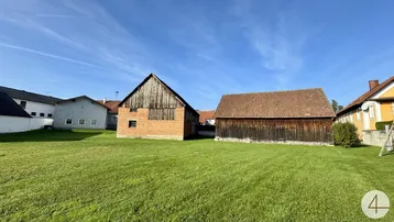 Ländliche Ansicht mit alten Scheunen und einem weitläufigen grünen Rasen unter blauem Himmel.