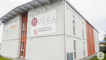 Modernes Motelgebäude mit schlichter Fassade, großen Werbebannern und mehreren Fenstern, umgeben von Grünflächen.