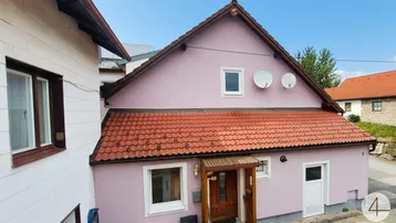 Nahaufnahme der rosa gestrichenen Hausfassade mit rotem Ziegeldach und traditionellem Eingangsbereich.
