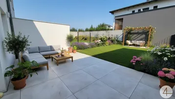 Gepflegter Garten mit großer Terrasse, bequemen Outdoor-Möbeln und blühenden Pflanzen.