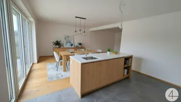 Moderne offene Küche mit Kochinsel und Essbereich, hell durch große Fenster mit Blick ins Grüne.