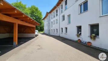 Außenansicht eines modernen Mehrfamilienhauses mit Carport und grüner Umgebung.