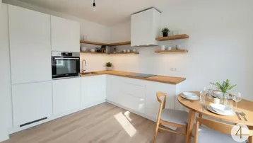Moderne Einbauküche mit weißen Fronten, Holz-Arbeitsplatte und Essbereich, hell beleuchtet.