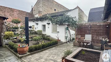 Kleiner, gepflasterter Innenhof mit Gartenbereich, Sitzgelegenheiten und einem Nebengebäude.
