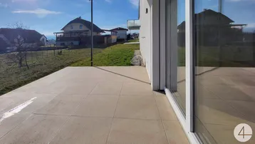 Große geflieste Terrasse mit Blick auf die umliegende Grünfläche und Nachbarhäuser.
