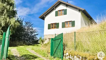Traditionelles Landhaus mit weißer Fassade, grünen Fensterläden und Zufahrt im Grünen.