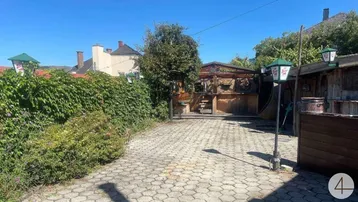 Gepflasterter Außenbereich mit Holzstrukturen, viel Grün und Laternen, ideal für gesellige Stunden im Freien.