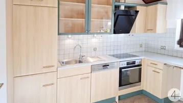 Helle Einbauküche mit Holzfronten, modernen Geräten und weißen Fliesen.