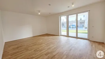 Helles Wohnzimmer mit Parkettboden und großen Glasfenstern zum Garten.