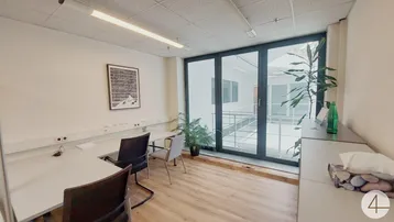Modernes Büro mit mehreren Arbeitsplätzen, Holzboden und großen Fenstern mit Blick auf einen Innenhof.