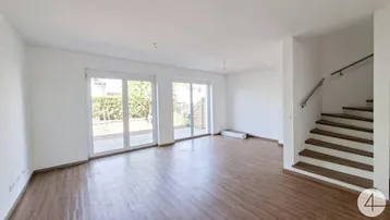 Helles, leeres Wohnzimmer mit Laminatboden, großen Fenstern und Treppenaufgang.