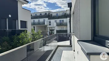 Moderner Balkon mit Glasgeländer und Blick auf die umliegenden Gebäude unter blauem Himmel.
