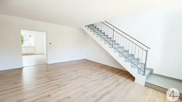 Heller Wohnbereich mit Laminatboden und offener Treppe, die in die obere Etage führt.