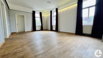 Geräumiges Wohnzimmer mit hellem Parkettboden, hohen Decken und großen Fenstern.
