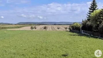 Weitläufige Grünfläche mit Blick auf Felder und Hügel unter blauem Himmel.