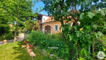 Charmantes Haus mit orangefarbener Fassade, umgeben von einem üppigen Garten und hohen Bäumen.
