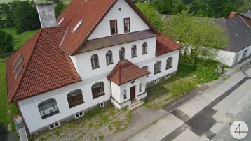 Luftaufnahme eines weißen Gebäudes mit rotem Ziegeldach und mehreren Fenstern, umgeben von Grünflächen.
