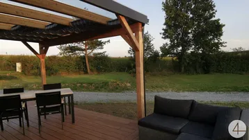 Geräumige Holzterrasse mit Pergola, Essbereich und Lounge-Möbeln, umgeben von grüner Natur.